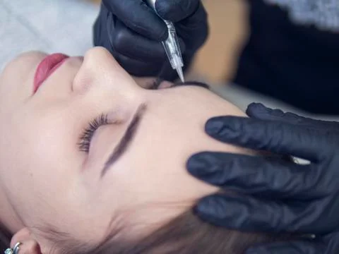 Microblading eyebrows workflow in a beauty salon. Light brown girl do eyebrows Stock Photos