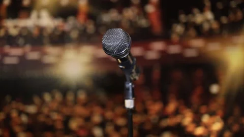A microphone in focus with a blurred audience and bright stage lights in the bac Stock Footage 293469828