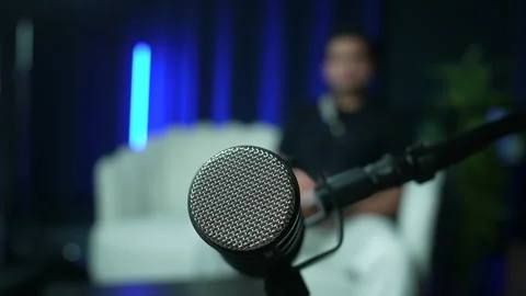 Microphone in Focus with Person Seated on Sofa in Modern Studio Interview Setup Stock Footage 336186594