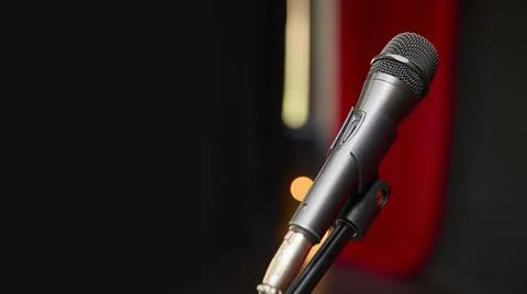 A microphone is positioned on a stand in front of a striking red curtain. A Stock Photos