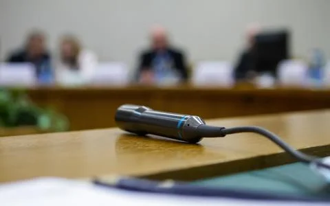 A microphone sits on a wooden table while people engage in discussion in the Foto stock