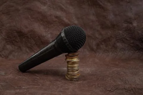 Microphone on a stack of coins on brown leather background, podcast revenue.. Stock Photos