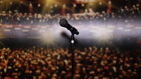 A microphone on a stand in front of a blurred audience and spotlight, creating a Stock Footage 293469851