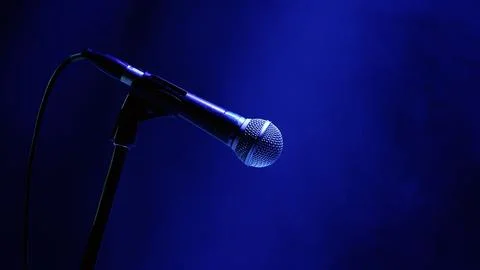 Microphone on stand under blue stage lighting with bokeh background Stock Photos