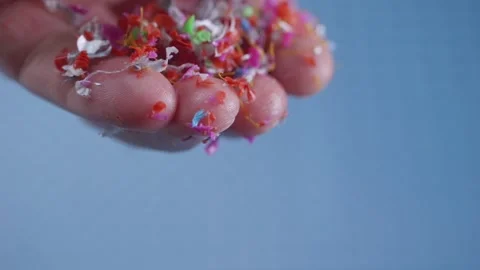 Microplastic fragments drift down from fingertips, vibrant particles slowly.. Vidéo 291096135