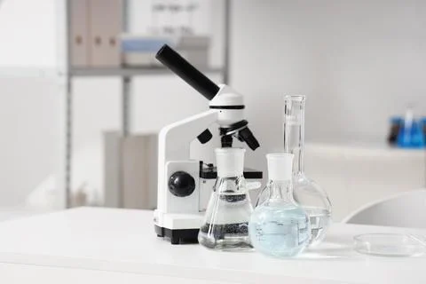 Microscope and flasks of water samples on table in research laboratory Фото