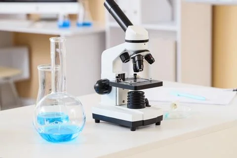 Microscope and laboratory glassware with blue liquid on table Stock Photos