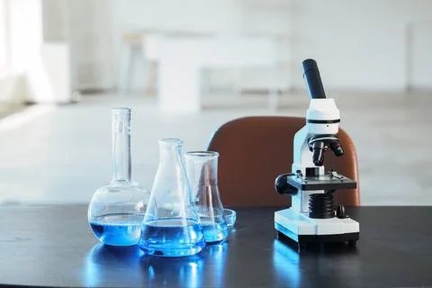 Microscope and laboratory glassware with blue liquid on dark table in science Stock Photos