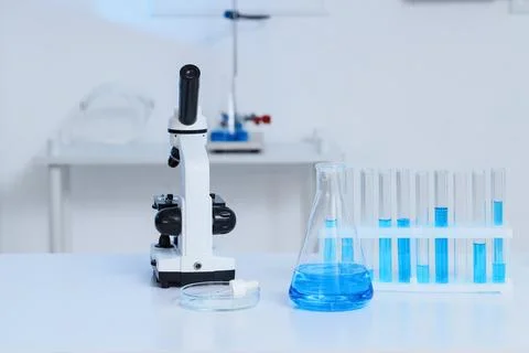 Microscope and laboratory glassware with blue liquid on a white table in a sc Stock Photos