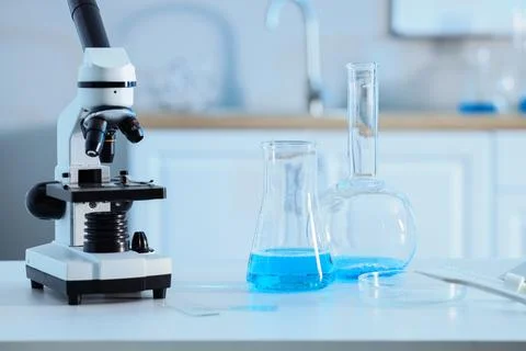 Microscope and laboratory glassware with blue liquid on white table in a mode Stock Photos
