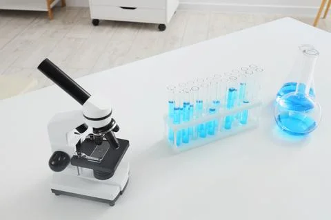 Microscope and test tubes with blue liquid on a white laboratory table, scien Stock Photos