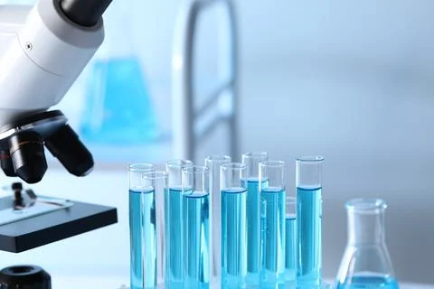 Microscope and test tubes with light blue liquid in laboratory, closeup Stock Photos
