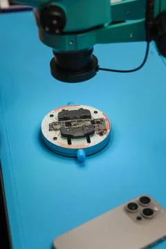 Microscope examining electronic circuit board on blue work surface with Stock Photos