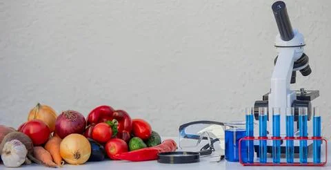 Microscope with fruits and vegetables on table Stock Photos