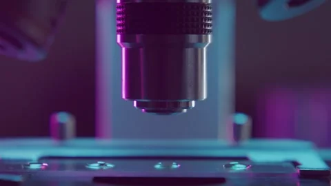 Microscope Lens Focusing on a Laboratory Slide Under Purple and Blue Lighting Vidéo 331110560