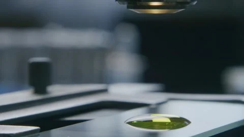 Microscope Lens Focusing on a Yellow Liquid Specimen on a Glass Slide Vídeos de archivo 331110532