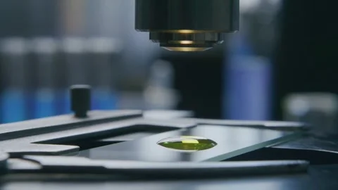 Microscope Lens Focusing on a Yellow Liquid Drop on a Glass Slide 库存影片 331110592