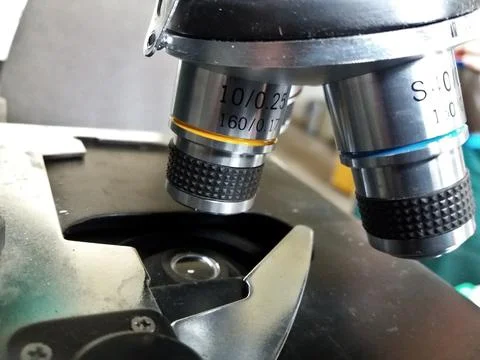 Microscope lens in the laboratory. Metal specimen clamp. Lens with yellow s.. Stockfoto's
