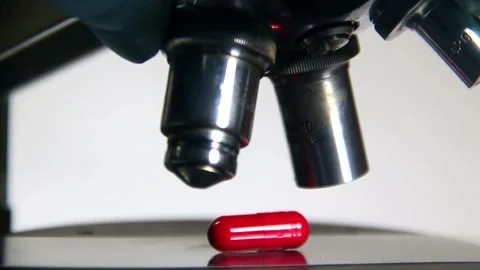 A microscope lens is lowered onto a pill and a doctor in a glove switches lenses Stock Footage 317310456