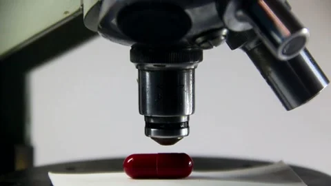 A microscope lens is lowered to a red pill and three lens switches Stock Footage 317296852