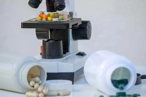 Microscope with pills and capsules on a lab table Stock Photos