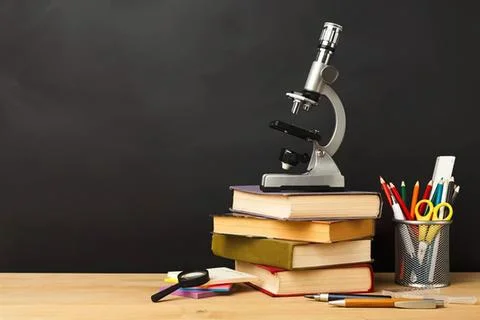 Microscope on stack of books with pens and ruler on desk Stock Photos