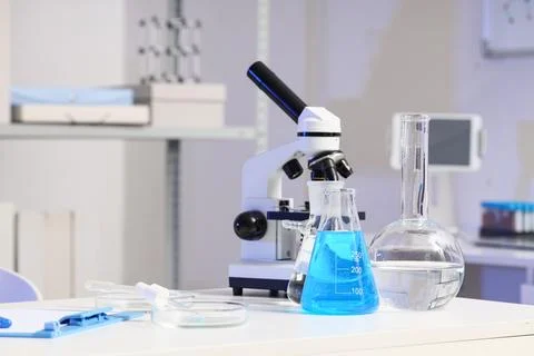 Microscope with test tubes and flasks of water samples on table in research l Фото