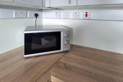 Microwave oven on modern kitchen worktop beneath wall cabinets and sockets Stock Photos