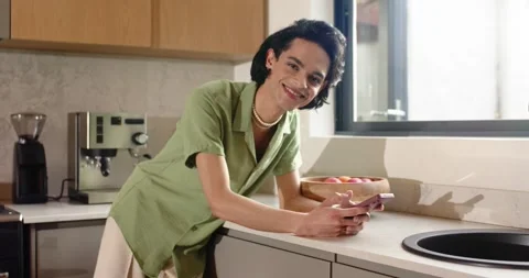 Mid-20s man grabbing smartphone after alert, scrolling on kitchen counter by Stock Footage 344534914