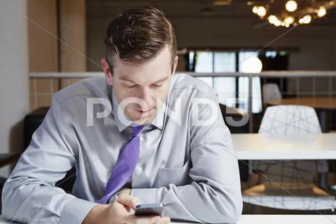 Mid Adult Businessman Sitting At Desk, Looking At Smartphone