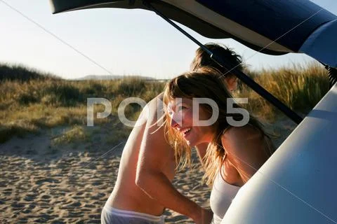 Mid Adult Couple Changing Clothes From Car On Beach