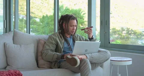 Mid adult man with dreadlocks receiving smartphone call while using laptop, Stock Footage 336715497
