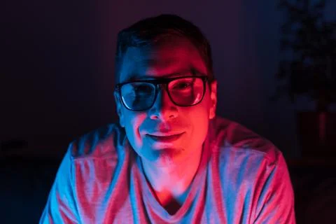 Mid adult man with glasses in neon light dark room Stock Photos