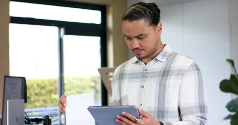 Mid adult man studying tablet at office standing desk by window retrieving Stock Footage 344333359
