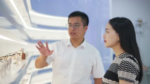 Mid-age consultant man in optical store helps to choose glasses for young woman Stock Footage 195140867