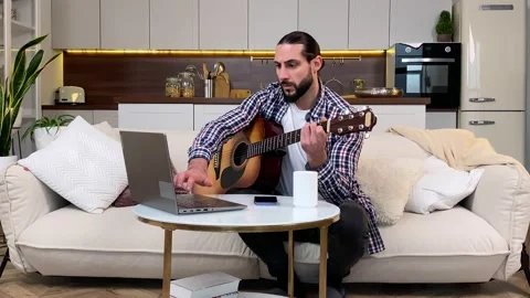 Mid aged bearded man learning play guitar by video tutorial indoors Stock Footage 229796306