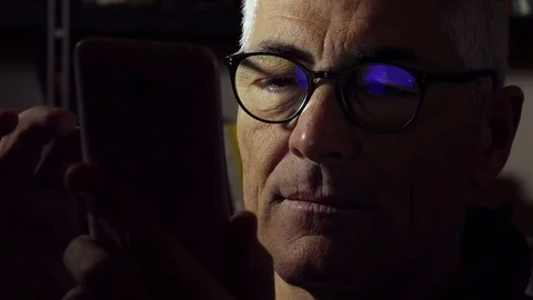 Mid aged man using cell phone and reflecting the screen over his glasses Stock Footage 74430898
