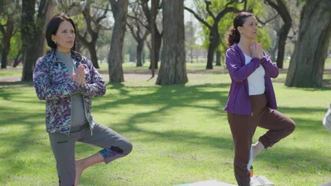 Mid-Aged Women Standing in Tree Pose on Yoga Practice with Coach Stock Footage 260210810