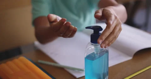 Mid section of boy sanitizing his hands while sitting on his desk at school Stock Footage 139516597