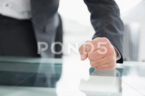 Mid section of businessman with clenched fist on office desk Stock Photos