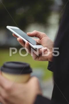 Mid Section Of Businesswoman Using Mobile Phone While Holding Disposable Coff