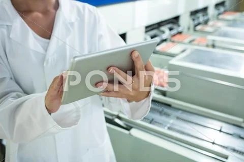 Mid Section Of Female Staff Using Digital Tablet Next To Production Line