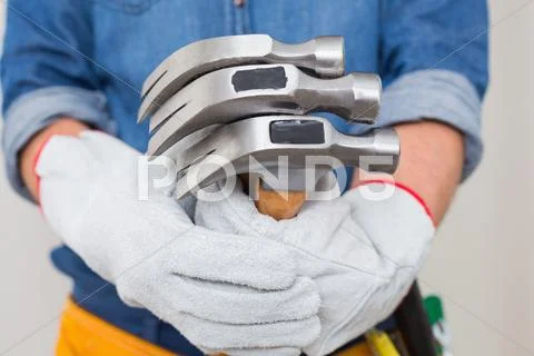 Mid section of a handyman holding hammers with toolbelt around waist Stock Photos