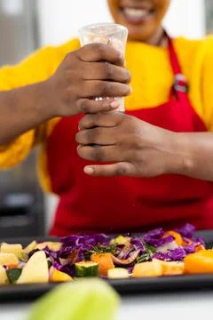 Mid section of happy plus size african american woman in apron seasoning Photos