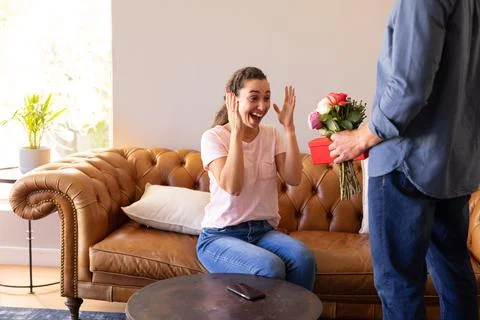 Mid section of a man surprising his wife with a flower bouquet and gift box at 写真素材