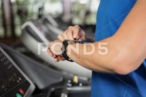 Mid Section Of Man Using Smart Watch On Treadmill At Gym