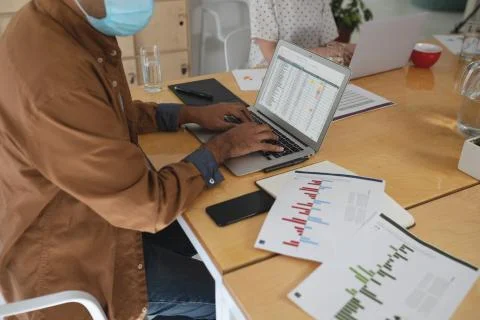 Mid section of man wearing face mask using laptop at office Stock Photos