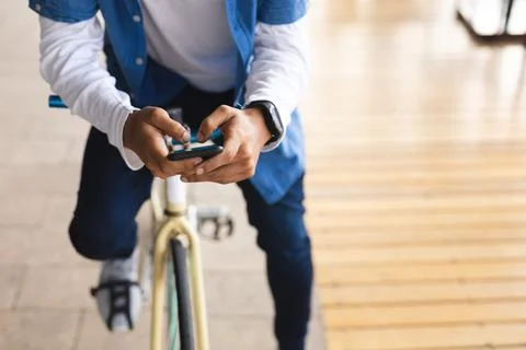 Mid section of mixed race man sitting on bicycle in street using smartphone Fotos Stock