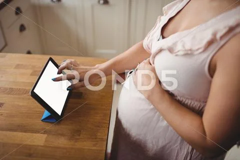 Mid Section Of Pregnant Woman Using Digital Tablet In Kitchen
