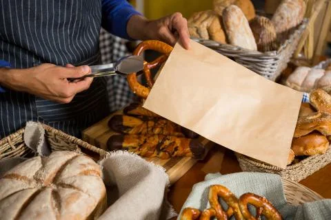 Mid section of staff packing pretzel bread in paper bag at counter Stock Photos